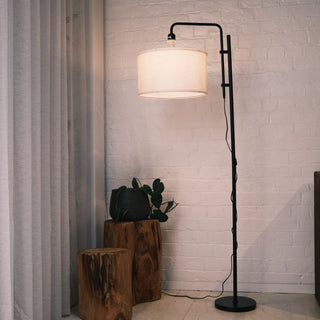 Modern black standing lamp with a warm fabric drum shade placed beside natural wood stools and indoor plants in a minimalist New Zealand living room. Showcasing floor lamps, standing lamps, modern floor lamps and dimmable lamps. | C&F Creation NZ