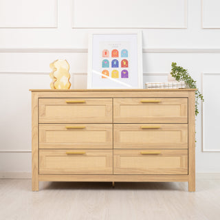 Front view of the Raya 6 Drawer dresser in warm oak finish, styled with brass handles and rattan drawer panels, set in a modern interior with wall art and decor on top.