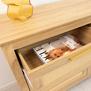 Close-up of the Raya six drawer tallboy in warm oak finish, showing an open drawer neatly storing a fashion magazine. The rattan-style drawer fronts and golden handles highlight the cabinet’s stylish design and practical storage for bedrooms or living spaces.