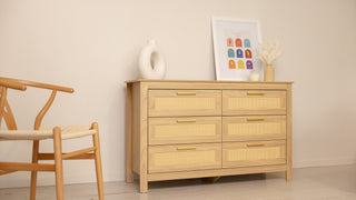 Raya 6-drawer lowboy dresser in natural oak with woven rattan drawer fronts and gold handles, styled in a neutral living room (123 × 40 × 75 cm).
