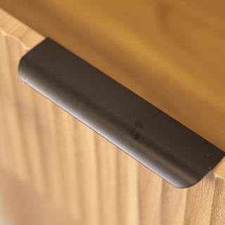 Close-up of the Reede Tallboy 5-Drawer handle in matte black, attached to the oak wood front, showing the smooth grip design and natural wood grain texture.