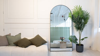 Renley arched full-length mirror with engraving detail, styled against a white wall beside a sofa and indoor plant – perfect for bedroom or hallway décor.