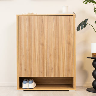 Front view of the Renne shoe cabinet in oak finish with closed double doors and an open bottom shelf displaying a pair of sneakers, ideal for modern entryway storage.