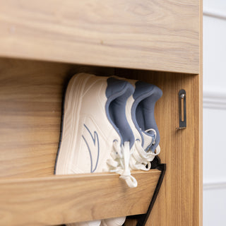 Close-up of the Risa slim shoe cabinet in oak finish showing a tilt-down compartment with white sneakers neatly stored, highlighting practical shoe storage and modern design.