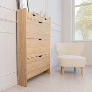 Side angle of the Risa Slim Shoe Cabinet in oak finish, placed beside a cream accent chair and window. The slim design and tall profile highlight its space-saving style, ideal for narrow entryways or modern living spaces.