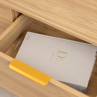 Close-up of the Ruelle 6 Drawer dresser in oak finish, featuring a brass gold handle and an open drawer holding a Dior Catwalk book. The image highlights the dresser’s storage function and smooth wood grain detail.
