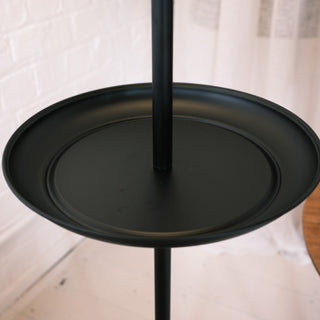 Close up of the Slate Tray Floor Lamp’s round matte black metal tray table, showing the smooth raised edge and central support pole against a soft interior background.

