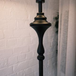 Close up view of the Slate Tray Floor Lamp’s sculpted matte black metal stem, showing the smooth curves and textured finish against a soft white brick wall background.
