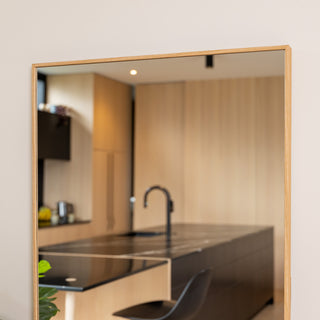 Close-up of the Solene X full-length mirror showing its 45 mm deep wooden PS frame in a natural oak tone. The mirror’s double silver glass reflects a modern kitchen with light wood cabinetry and a black island, highlighting the mirror’s clarity and warm, minimalist design.