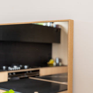Close-up of the Solene X full-length mirror showing the 45 mm wooden PS frame with smooth edges and a natural oak texture. The 4 mm double silver glass reflects a modern kitchen interior with black cabinetry and light wood finishes, highlighting the mirror’s clarity and fine craftsmanship.