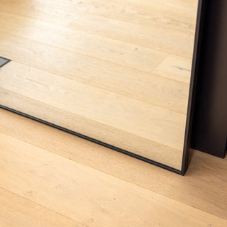 Close-up view of the Titan X arched full-length mirror resting on a light timber floor. The slim 32 mm aluminium frame showcases its precise craftsmanship and sturdy edge finish, highlighting the mirror’s sleek design and stable floor-standing structure.