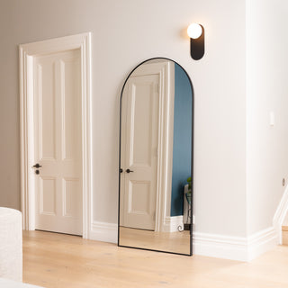 The Titan X arched full-length mirror elegantly mounted on a neutral-toned wall beside classic white doors and timber flooring. Its slim 32 mm aluminium frame complements the modern minimalist interior, reflecting natural light and adding depth to the hallway.