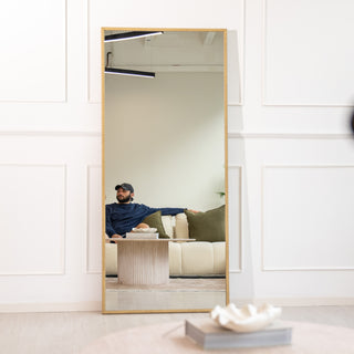 Tresson full-length mirror 180x80cm with a sleek gold PS frame and clear 4mm glass, reflecting a stylish living room with a cream sofa and green cushions. Perfect as a wall-mounted or floor mirror, this elegant piece adds warmth and sophistication to contemporary New Zealand interiors.