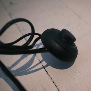 Close-up of the Trilogy 3-Light Floor Lamp's convenient foot pedal switch. The durable black control button allows for easy on-off operation without bending down. Attached to a sturdy power cord for functional reach.
