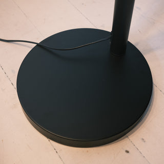 The Trilogy 3-Light Floor Lamp's sturdy circular base plate. Constructed from heavy matte black metal to ensure stability and prevent tipping. Features a neat cable exit point near the central pole.