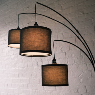 Trilogy 3-Light Floor Lamp featuring three staggered drum shades. The black woven fabric texture is clearly visible. Elegant curved arms extend from a sturdy central pole. Functional ambient lighting for reading or relaxing.