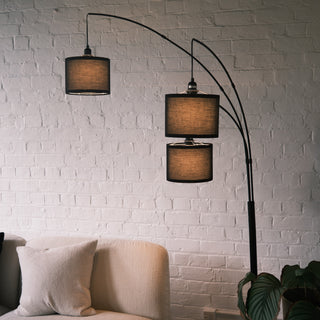 Side profile of the Trilogy 3-Light Floor Lamp highlighting the graceful curve of the matte black metal arms. Uniform textured fabric shades provide focused overhead lighting. Minimalist and functional lighting for a lounge area.