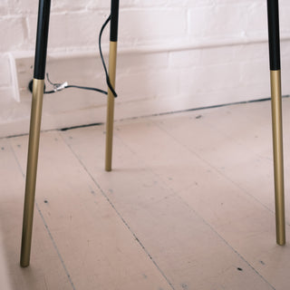 Close up of the Vanta floor lamp’s gold tipped legs on a light timber floor, showing the sleek black and brass contrast and minimal modern design.