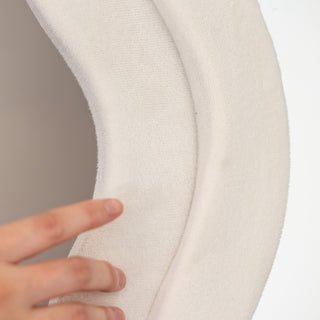 A close-up view of the Velora Wavy Mirror’s soft white velvet frame, highlighting its plush texture and elegant wavy design. A hand gently touches the surface, showcasing the luxurious feel and high-quality craftsmanship of the mirror’s exterior.