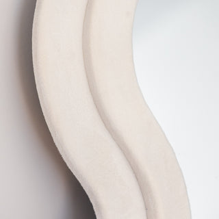 A close-up of the Velora Wavy Mirror’s plush velvet frame in soft ivory, showcasing its luxurious texture and smooth, curvy design. The high-quality fabric wrap enhances the elegant aesthetic, making it a standout statement piece for modern interiors.