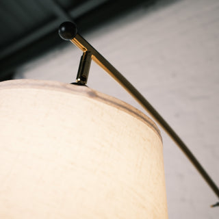 Close up of the Vienna Brass Floor Lamp showing the curved brass arm, black end cap, and the top edge of the cream fabric lampshade against a soft indoor backdrop.
