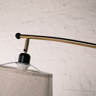 Close up of the Vienna Brass Floor Lamp showing the brushed brass top arm, black bulb holder, and shade fitting frame against a soft white brick wall background.
