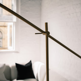Close up of the Vienna Brass Floor Lamp’s adjustable arm joint, showing the brushed brass finish and control lever, with a soft living room background featuring a white sofa and black cushion.
