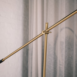 Close up of the Vienna Brass Floor Lamp’s adjustable arm and pivot joint, showing the brushed brass finish and refined hardware against soft curtains and a white brick wall.
