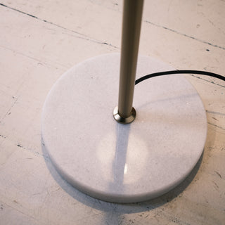 Close up of the Vienna Brass Floor Lamp’s round white marble base with a brushed brass pole and visible power cord, sitting on a lightly textured timber floor.

