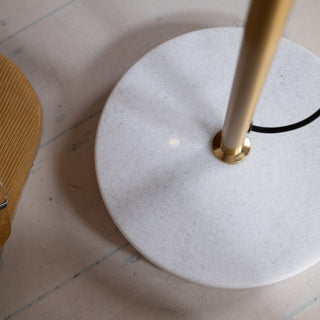 Close up of the Vienna Brass Marble Base Floor Lamp showing the solid white marble base and brushed brass pole. A hint of a mustard upholstered chair appears beside it, set on a light timber floor in a modern New Zealand home.