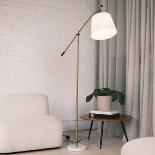 Vienna Brass Marble Base Floor Lamp displayed beside a cream sofa and wooden side table, featuring a brushed brass frame, adjustable arm, and white marble base. A stylish floor lamps nz option ideal for modern homes. Keywords include floor lamps nz, standing lamps, modern floor lamps, dimmable lamps.
