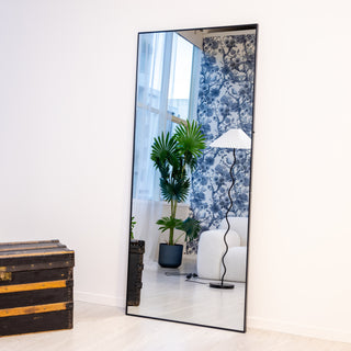 Modern 180x80cm Zenith X full-length mirror leaning against a white wall, showcasing its straight-edge black frame and clear reflection in a stylish interior.
