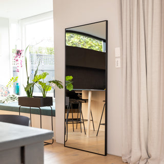 Zenith X full-length mirror (180 x 80 cm) with a sleek 30 mm aluminium alloy frame and ultra-clear 3 mm glass, reflecting a bright, modern living space with greenery and natural light. The mirror stands elegantly against a wall beside flowing curtains, enhancing depth and sophistication in the room.