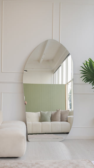 Cascade X irregular frameless full-length mirror standing in an NZ living room, reflecting cream couch and sage green wall panel, C&F Creation